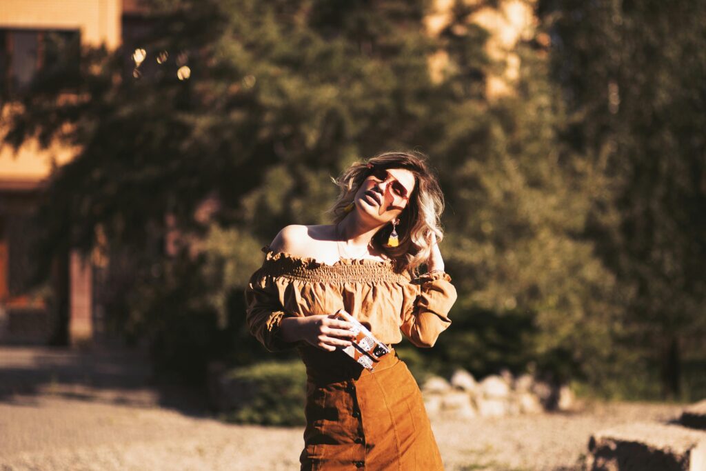 Fashionable woman posing outdoors with sunglasses in warm sunlight, embodying summer style.