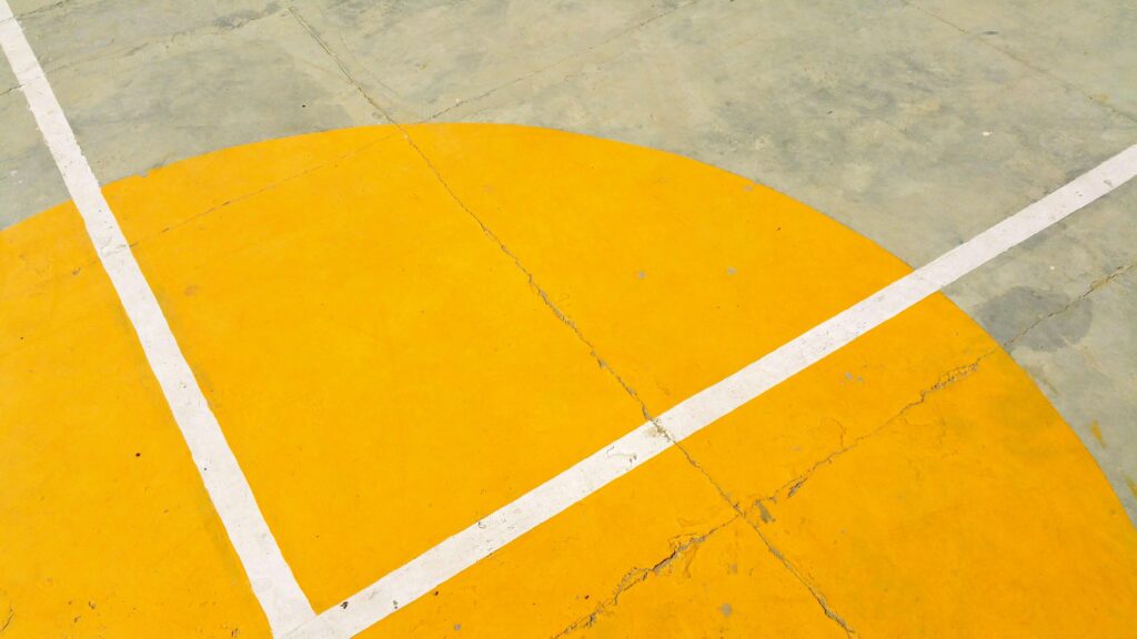 Close-up of a basketball court with yellow semicircle and white lines on concrete surface.