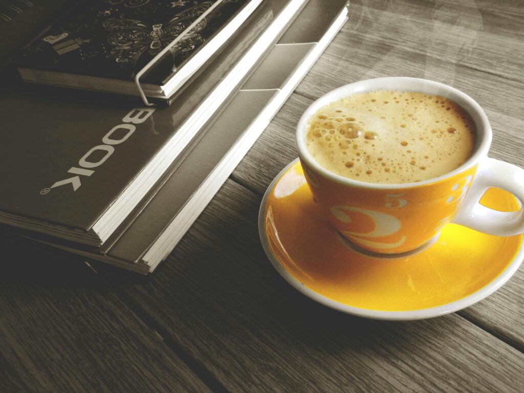 A warm cup of coffee on a yellow saucer beside a stack of books, perfect for a relaxing break.