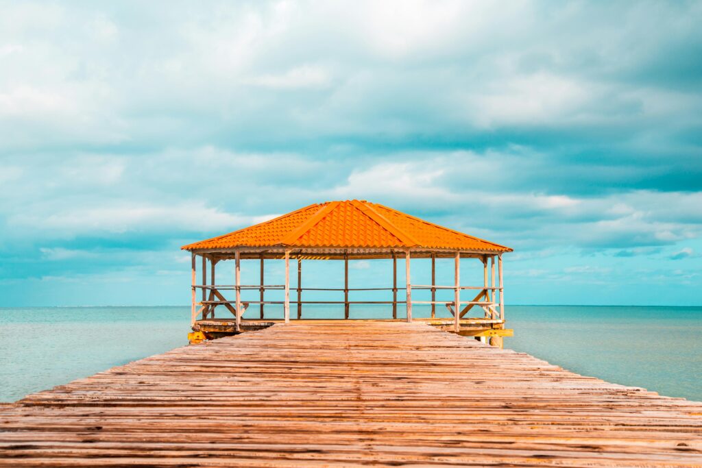 Wooden pier leading to a gazebo by the turquoise sea under a vibrant sky.